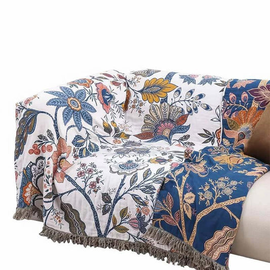 Reversible Cotton Throw Blanket with white and blue floral pattern, fringe edge draped over sofa in living room.