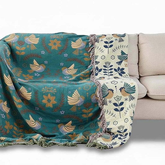 100% Cotton Reversible Throw Blanket on a beige sofa in a living room; teal bird pattern with light cream reverse.